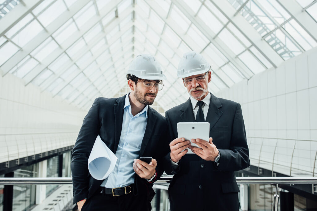 two-successful-entrepreneur-helmet-with-project-laptop-new-buildings-stay-near-glass-roof-scaled.jpg